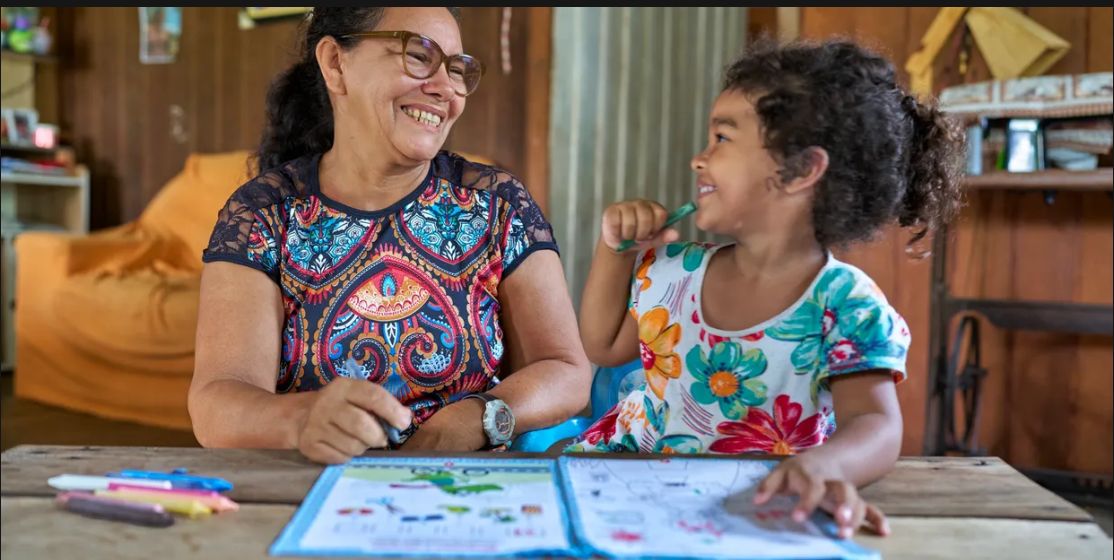 Grandmother and granddaughter smiling together over an educational workbook