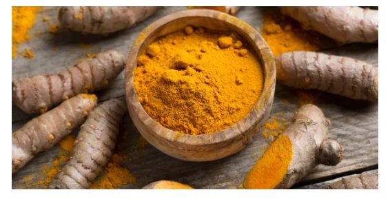 Bowl of ground organic turmeric surrounded by fresh turmeric root